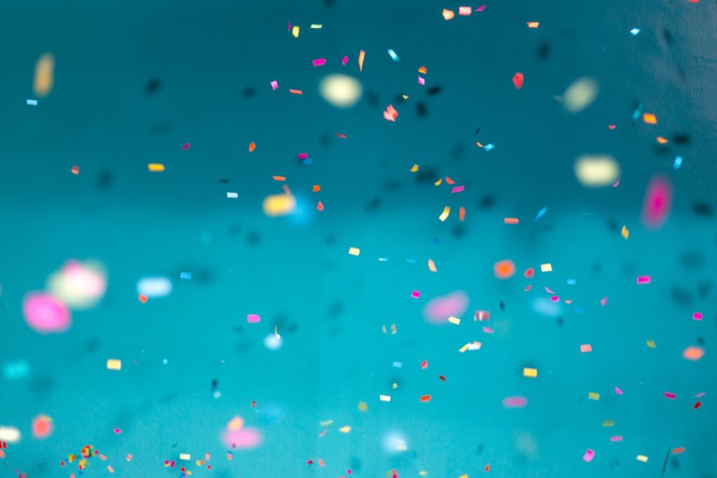 Colorful confetti falling on teal background, festive anniversary celebration atmosphere